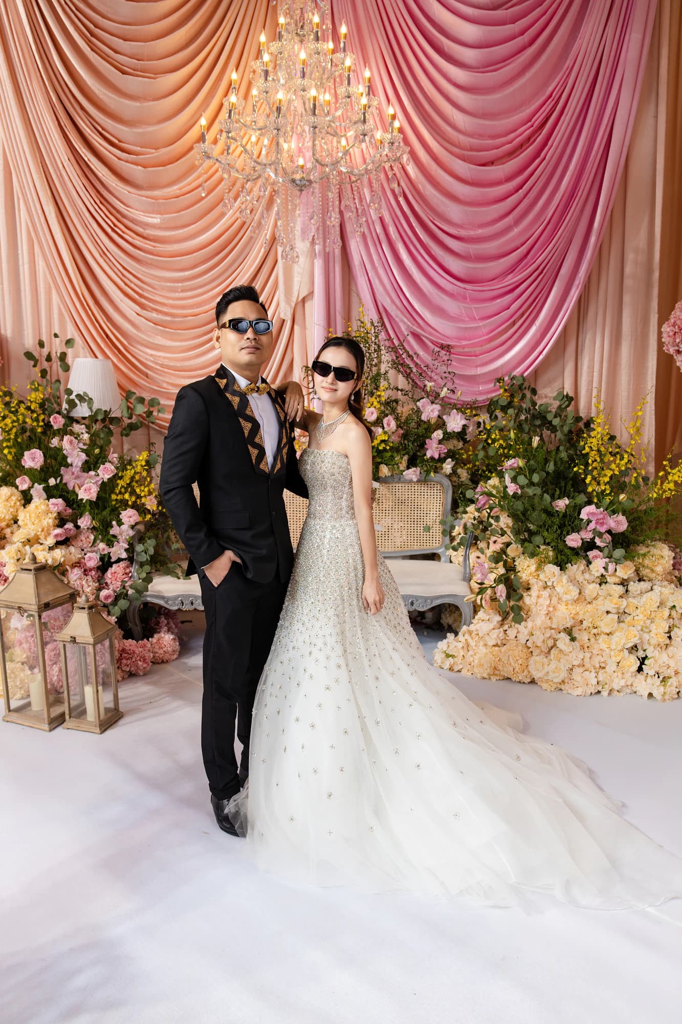 Sokvebol & Souhouy — គូស្វាមីភរិយាឈរជាមួយគ្នាក្រោមចង្កៀងព្យួរ ក្នុងឈុតខ្មៅ និងរ៉ូបពណ៌សប៉ាក់គុជ