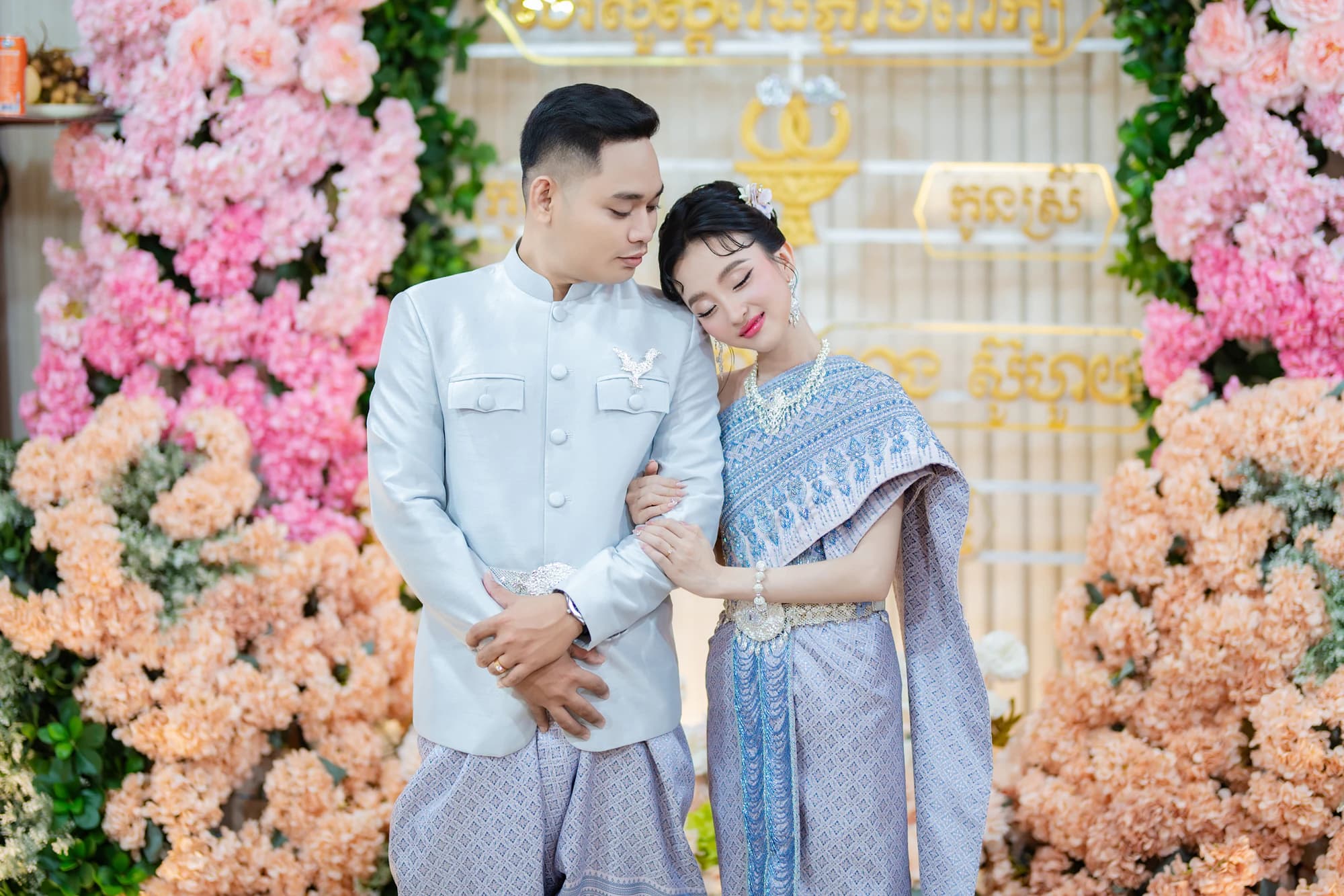 Sokvebol & Souhouy — គូស្វាមីភរិយាដៃក្នុងដៃក្នុងសំពត់សូត្រខ្មែរ ព័ទ្ធជុំវិញដោយផ្កាពណ៌ផ្កាឈូក និងទឹកក្រូច